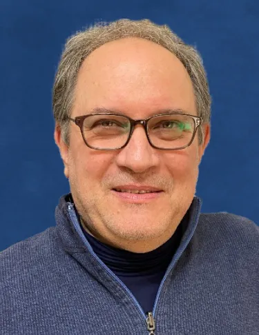 A man wearing glasses and a blue sweater with a blue backdrop background