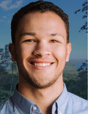 A smiling man in a blue shirt with a forest background